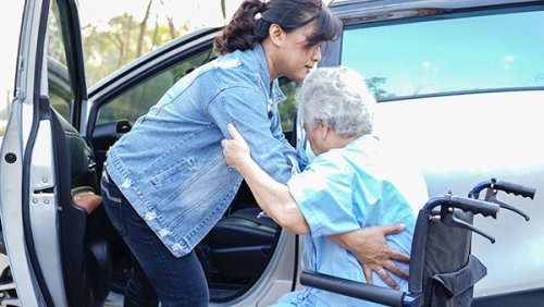 Woman helping a women in a wheelchair get up in the car